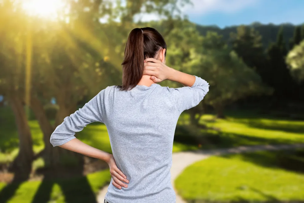 Woman practicing self-acupressure on her neck and lower back outdoors